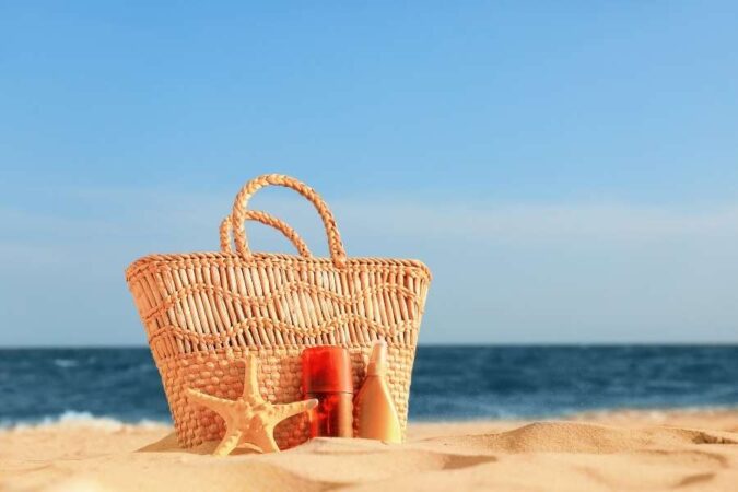Un sac de plage en osier posé sur le sable avec une étoile de mer et des produits solaires.