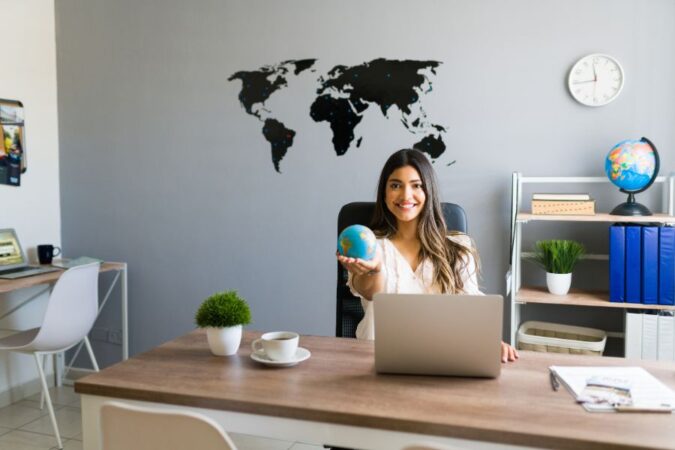 Une conseillère souriante tient un globe dans son bureau pour illustrer les agences de voyage traditionnelles.